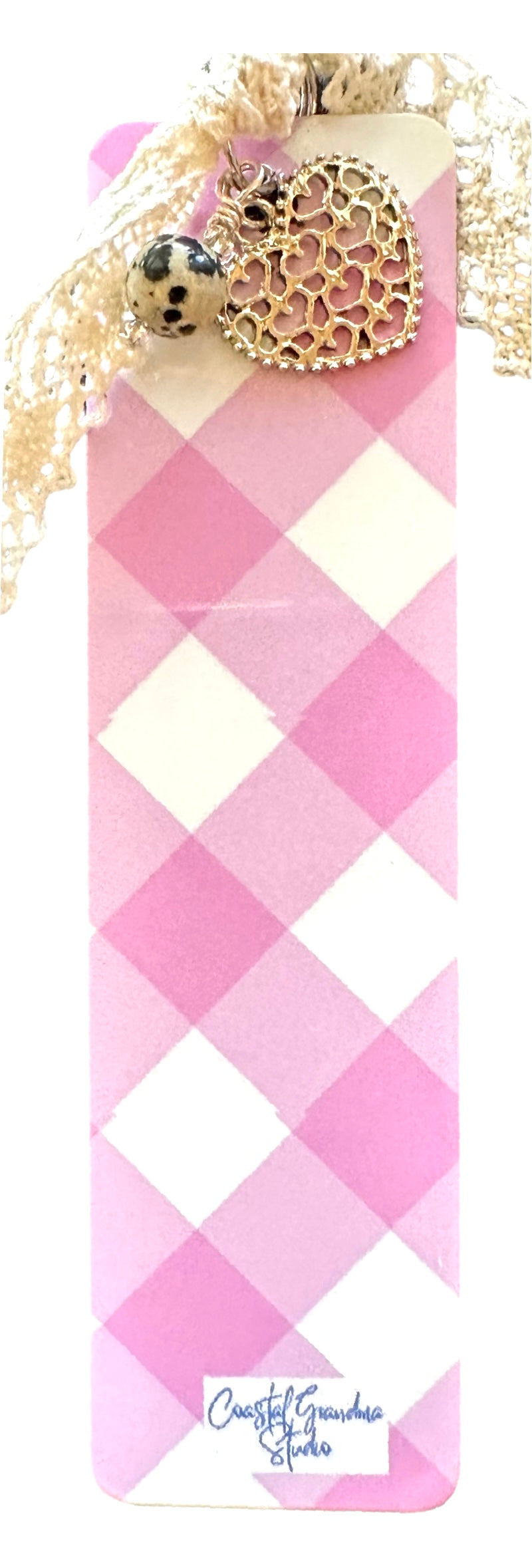 A lightweight aluminum bookmark with a pink gingham pattern, featuring a vintage lace ribbon and a dalmation jasper bead, tied with a string and a filigree heart charm.