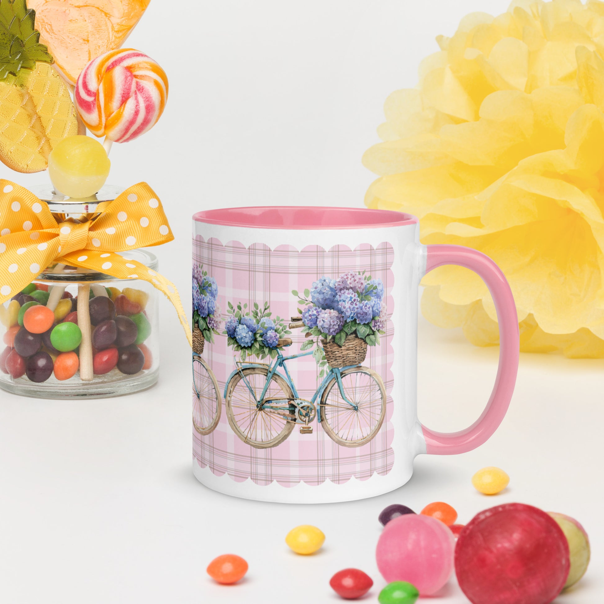White Mug with bicycle and flower design , pink interior and handle on a white background with candies and flowers.