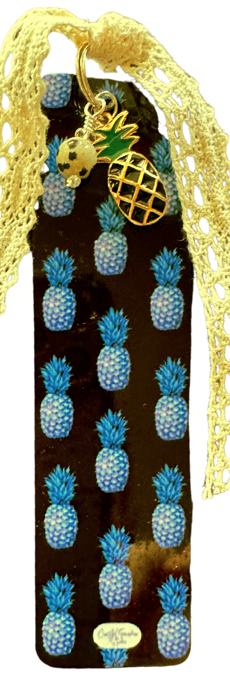 A bookmark featuring a vintage lace ribbon, a pineapple charm, and a Dalmation Jasper bead, all against a dark background with colorful  pineapple prints.