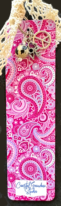 A vibrant orange and pink aluminum bookmark with a '70's Paisley' pattern, featuring vintage lace,peace sign and LOVE charms , and a Dalmation Jasper  bead, tied with a string.