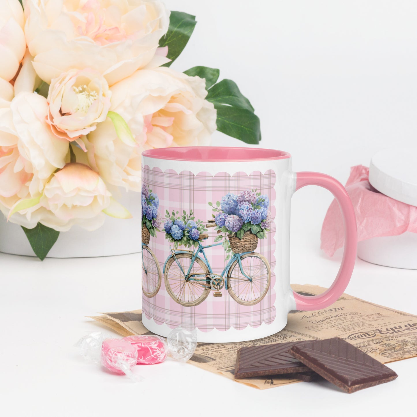 White Mug With Pink Handle and Interior with bicycle and flower design on a table with flowers and chocolate